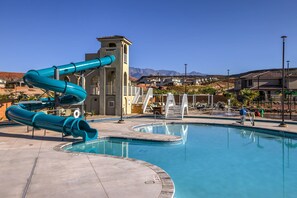 Une piscine avec un toboggan bleu, une petite tour et une vue sur les maisons au loin.