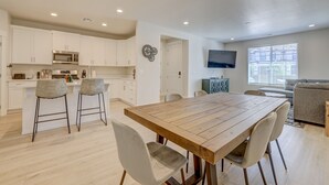 A modern kitchen with white cabinets, a wooden dining table, and bar stools. - Red Rock Oasis! Close to Adventure! Family Friendly! Amazing Pool! (Washington)