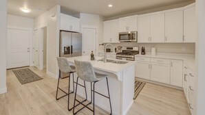 A modern kitchen with white cabinets, stainless steel appliances, and a central island with bar stools. - Red Rock Oasis! Close to Adventure! Family Friendly! Amazing Pool! (Washington)