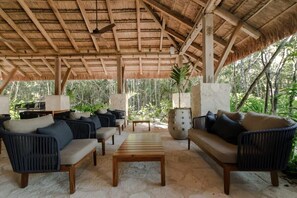 Relax in a shaded outdoor lounge with comfortable sofas and a central table, surrounded by lush vegetation.