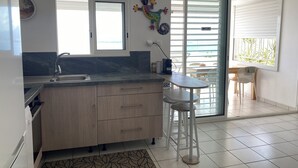 A modern kitchen with a sink, a wooden countertop, and a window. There is a chair and a table outside the window. - L'oiseau du Paradis, Charmant T2 Avec vue Imprenable (Les Trois-Îlets)