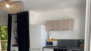 A compact kitchen with a washing machine, microwave, and a dining area with a table and chairs. - L'oiseau du Paradis, Charmant T2 Avec vue Imprenable (Les Trois-Îlets)