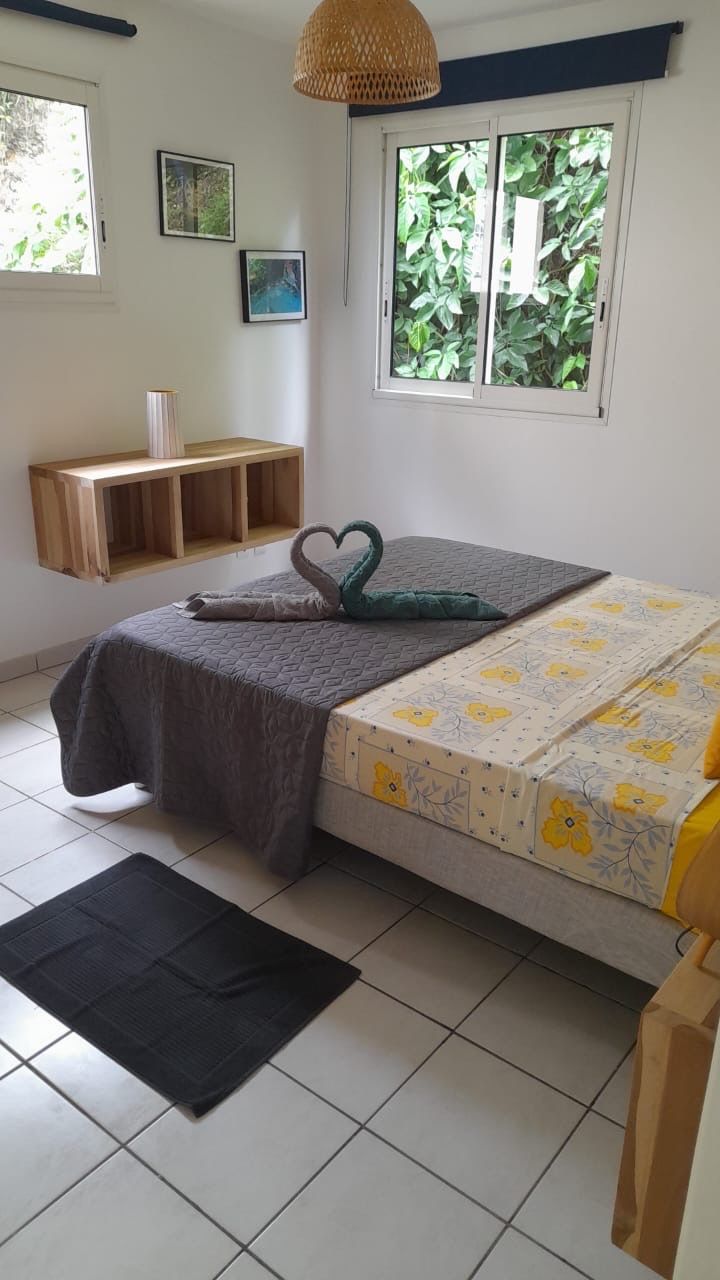 Een slaapkamer met een bed, een raam met uitzicht op groen, een nachtkastje en een zwevend plankje.