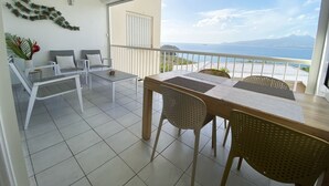 A balcony with a table and chairs, a ceiling fan, and a view of the sea. - L'oiseau du Paradis, Charmant T2 Avec vue Imprenable (Les Trois-Îlets)