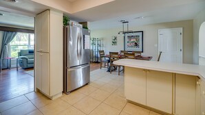 Una cocina moderna con un refrigerador empotrado, un comedor con mesa y sillas, y una sala de estar con sofá y ventana.