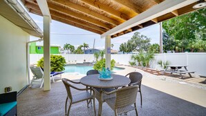 Un patio exterior con piscina, muebles de mimbre y techo de madera.