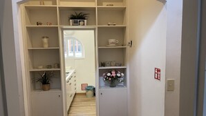 A narrow hallway with white shelving units, a small plant, and a vase of flowers.