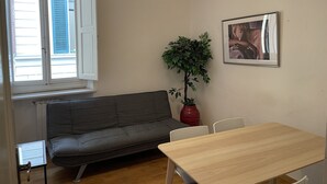 A room with a grey sofa, a wooden table, a potted plant, a hanging light fixture, and a framed picture on the wall.