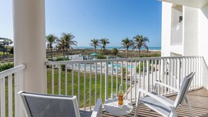 A balcony with a view of the beach, a pool area, and a table with a bottle and glasses. - Your Beach Escape Awaits (Treasure Island)