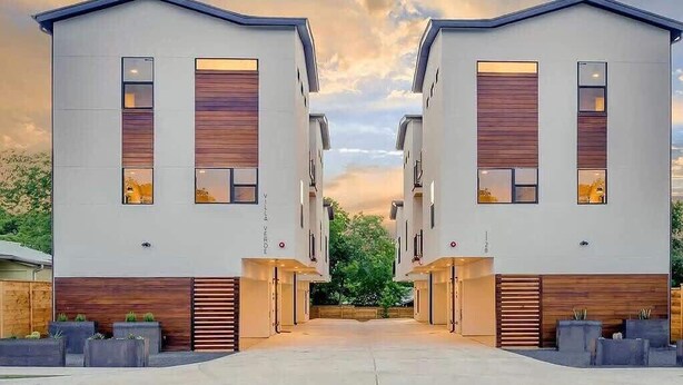 A modern residential building with a symmetrical design, featuring two-story structures with large windows and wooden panel accents.