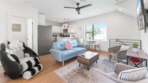 A modern living room with a sofa, armchair, and a coffee table. There is a kitchen area with cabinets and a refrigerator.