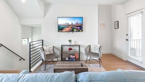 A modern living room with a cityscape TV, two armchairs, a coffee table, and a staircase.