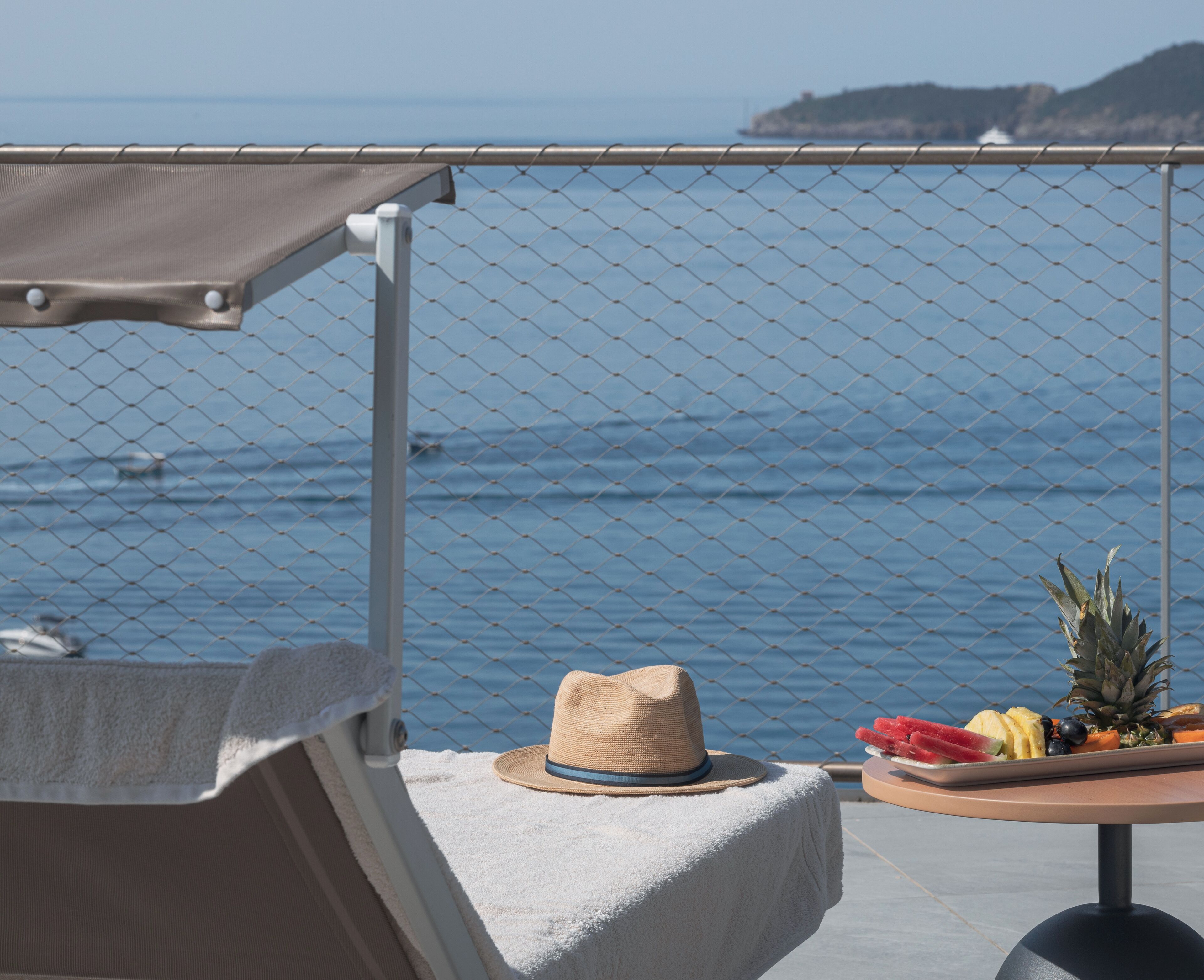 Un balcón con sombrero y fruta sobre una mesa, con vista al mar.