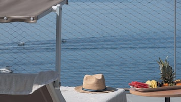 Un balcón con sombrero y fruta sobre una mesa, con vista al mar.