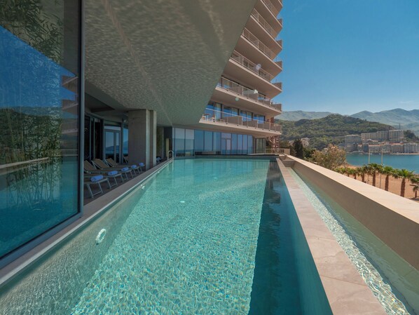 A modern hotel with a large outdoor swimming pool, a balcony with sun loungers, and a view of the sea and mountains. - Sea Star Budva (Rafajlovici)