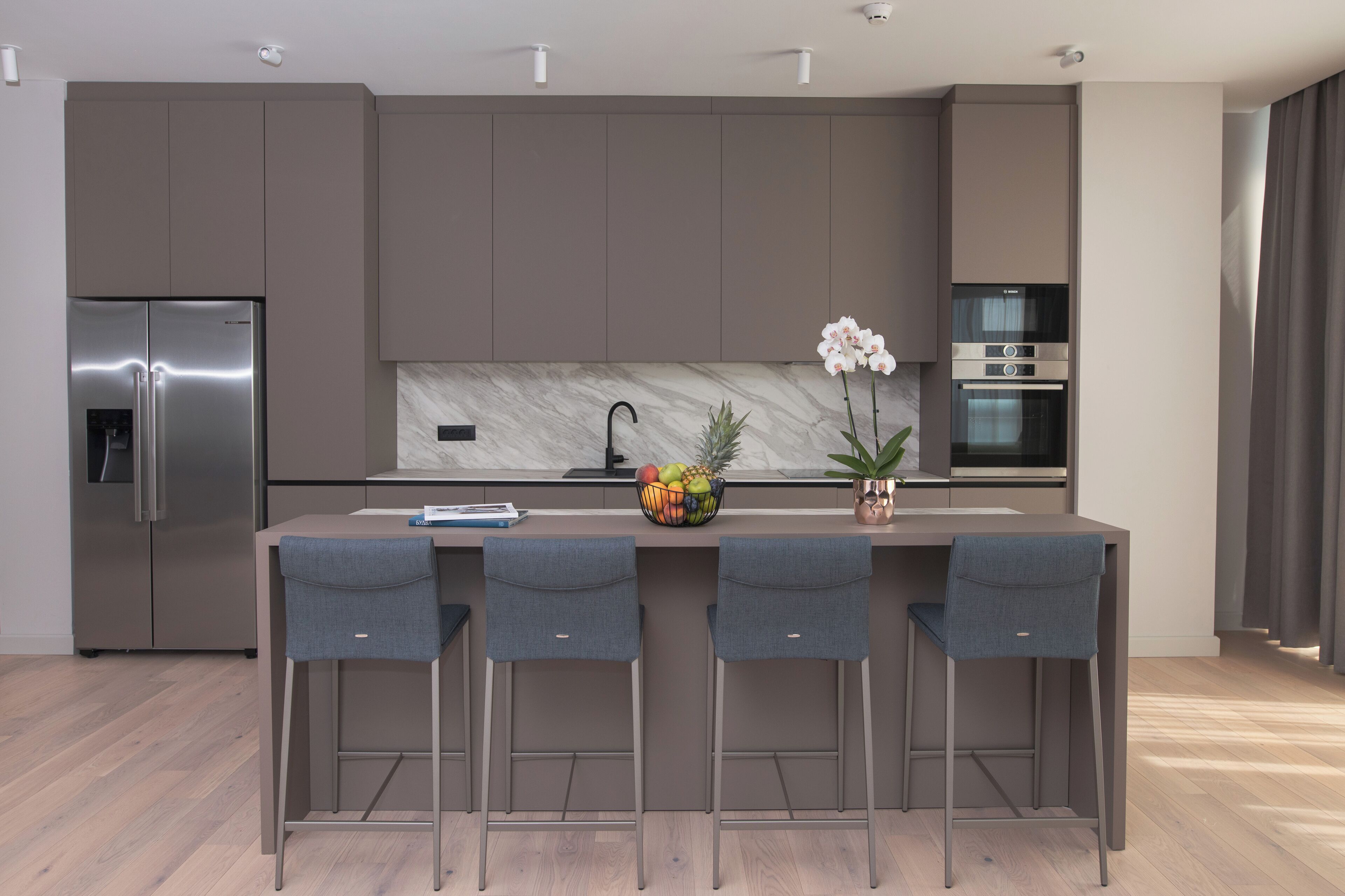 A modern kitchen with a marble backsplash, stainless steel appliances, and a central island with bar stools.