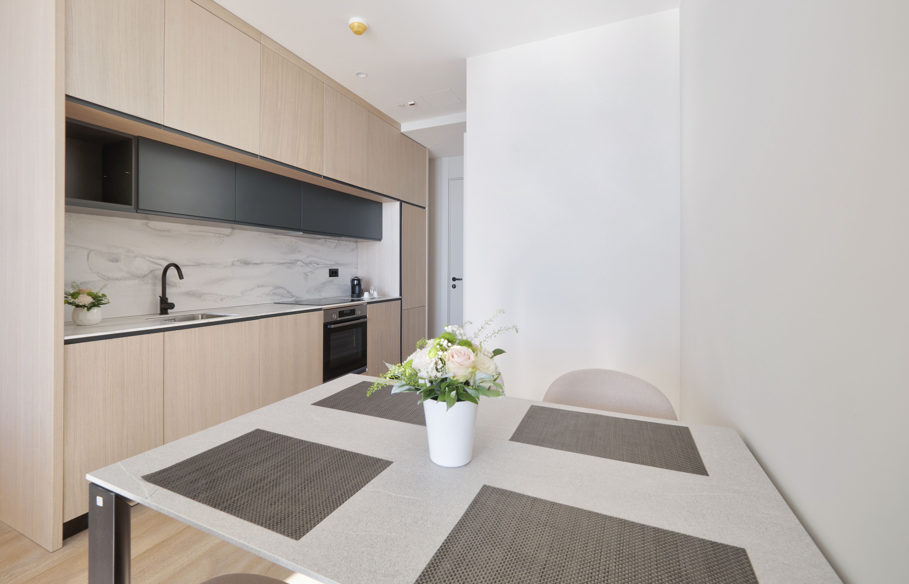 A modern kitchen with wooden cabinets, a marble backsplash, and a dining area with a table and chairs.