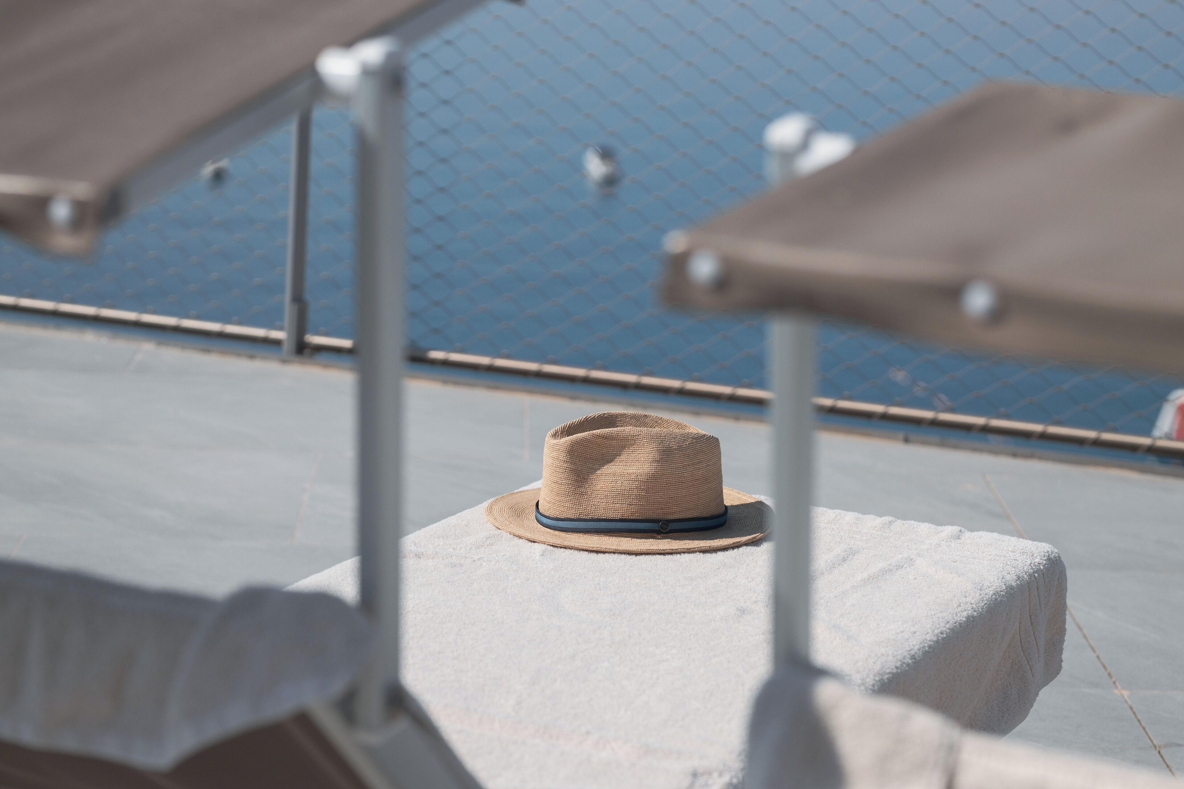 Un sombrero sobre una superficie blanca, con una cerca de malla y un cuerpo de agua al fondo.