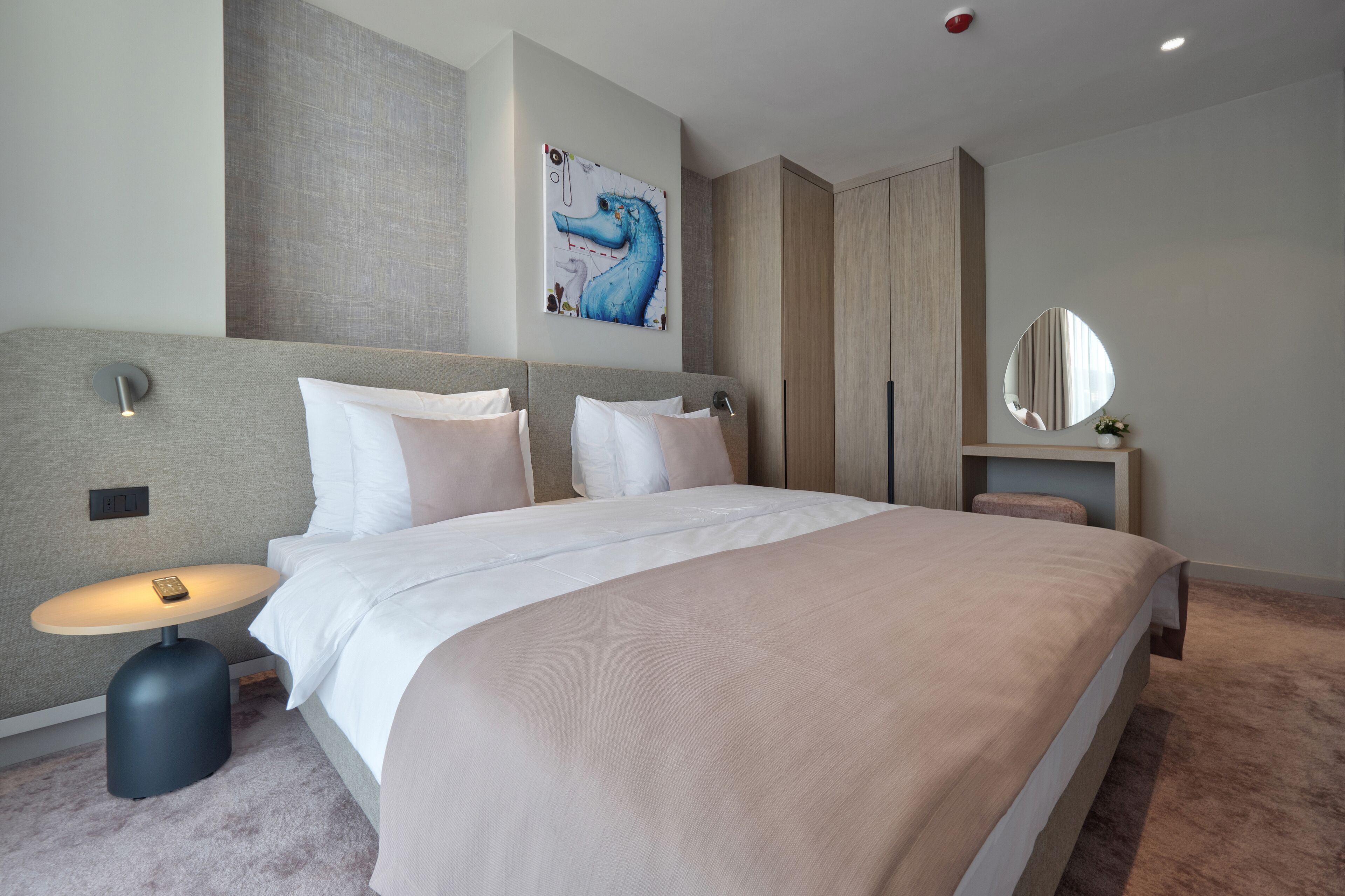 Een moderne hotelkamer met een groot bed, een nachtkastje met een lamp, een kunstwerk aan de wand en een spiegel.
