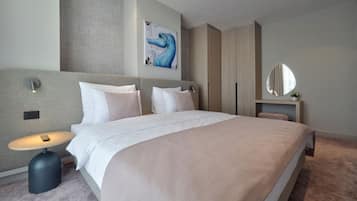 A modern hotel room with a large bed, a bedside table with a lamp, a wall-mounted artwork, and a mirror.