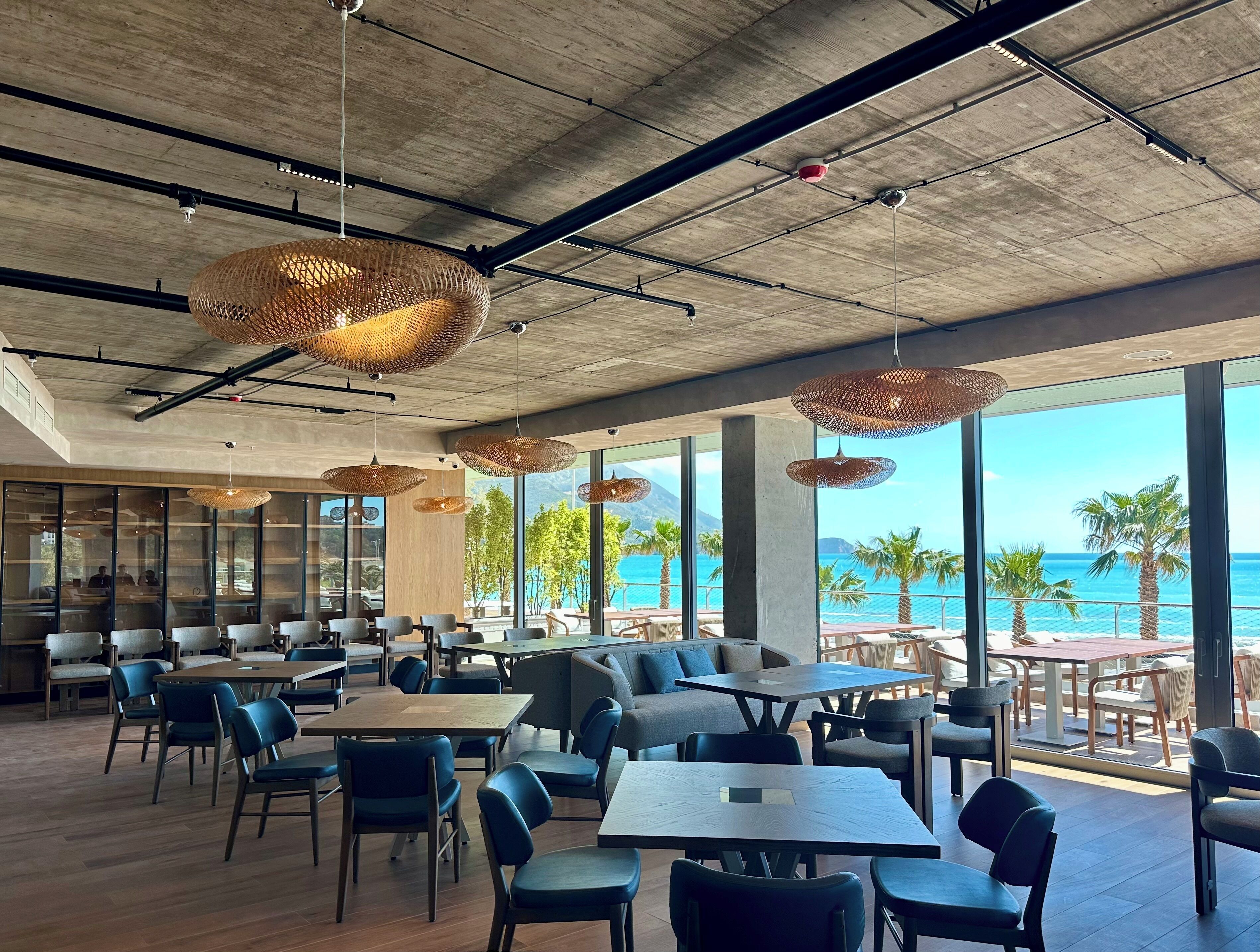 Un restaurante moderno con amplios ventanales que ofrecen vistas al océano, vigas de techo a la vista e iluminación colgante tejida.