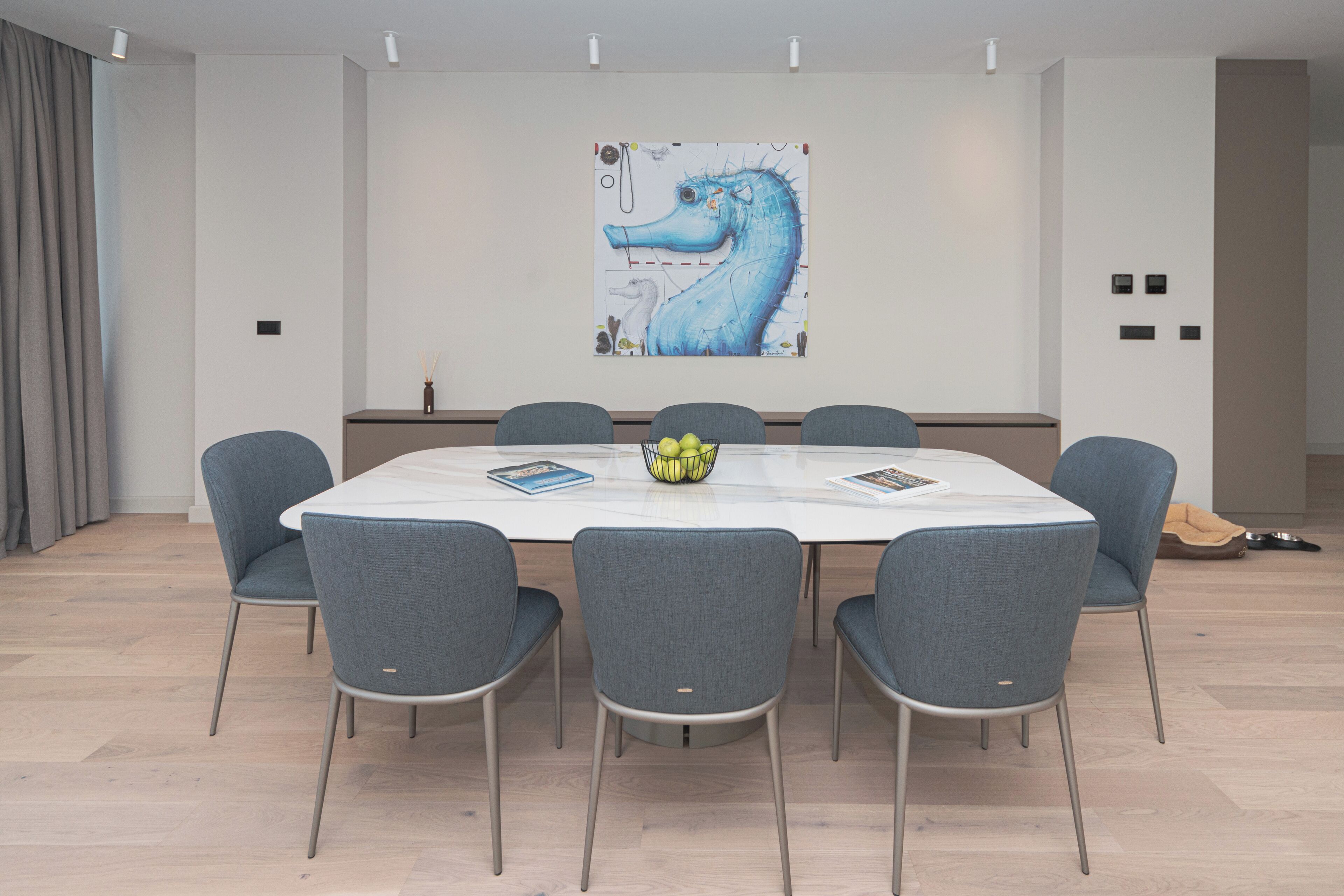 A modern meeting room with a white table, six grey chairs, and a large abstract painting on the wall.