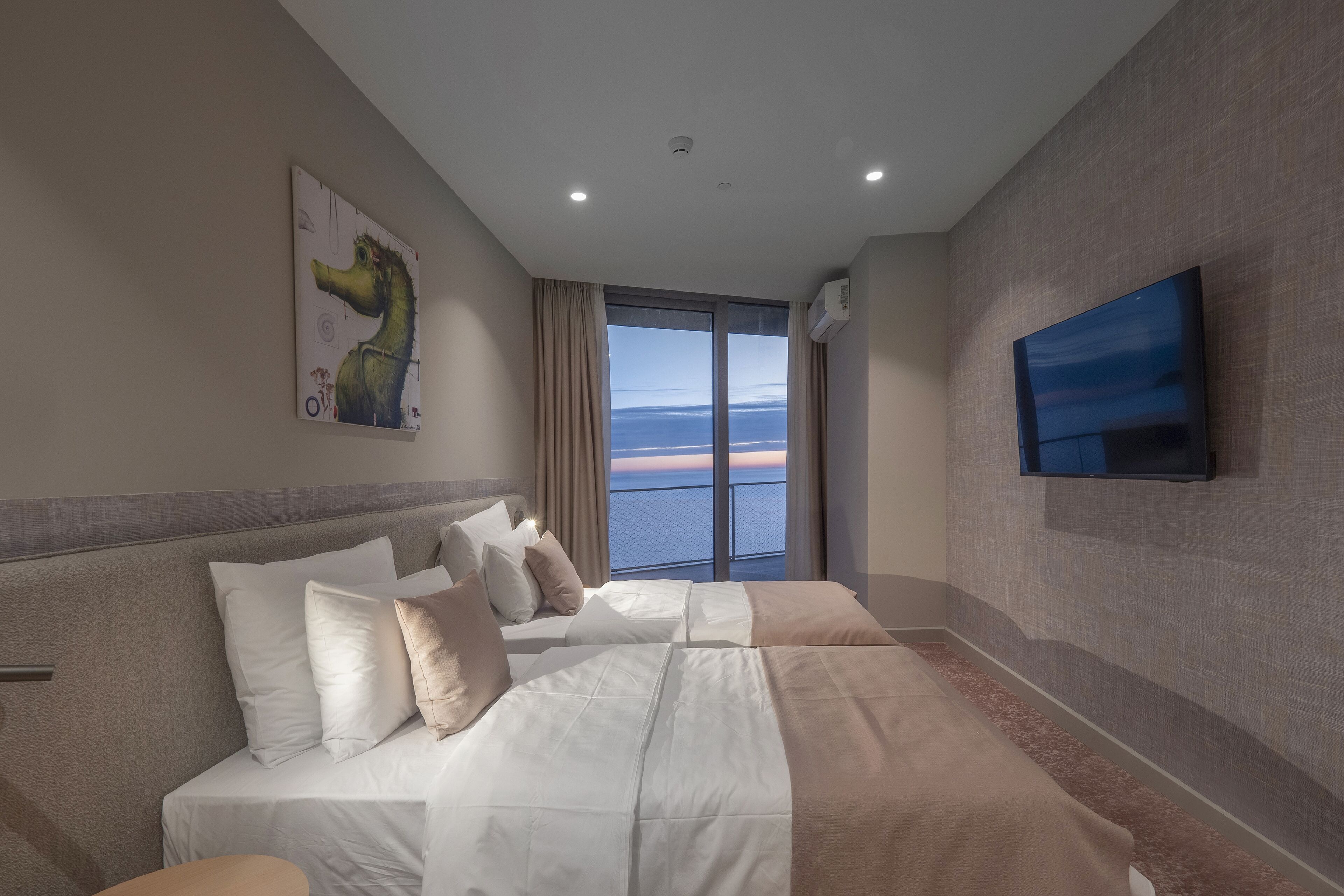 Habitación de hotel con una cama grande, un televisor en la pared y ventana con vistas al mar.