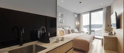 Ein modernes Hotelzimmer mit einem großen Bett, einer Küchenzeile mit Spüle und Kaffeemaschine, einem Flachbildfernseher und Blick auf den Strand.