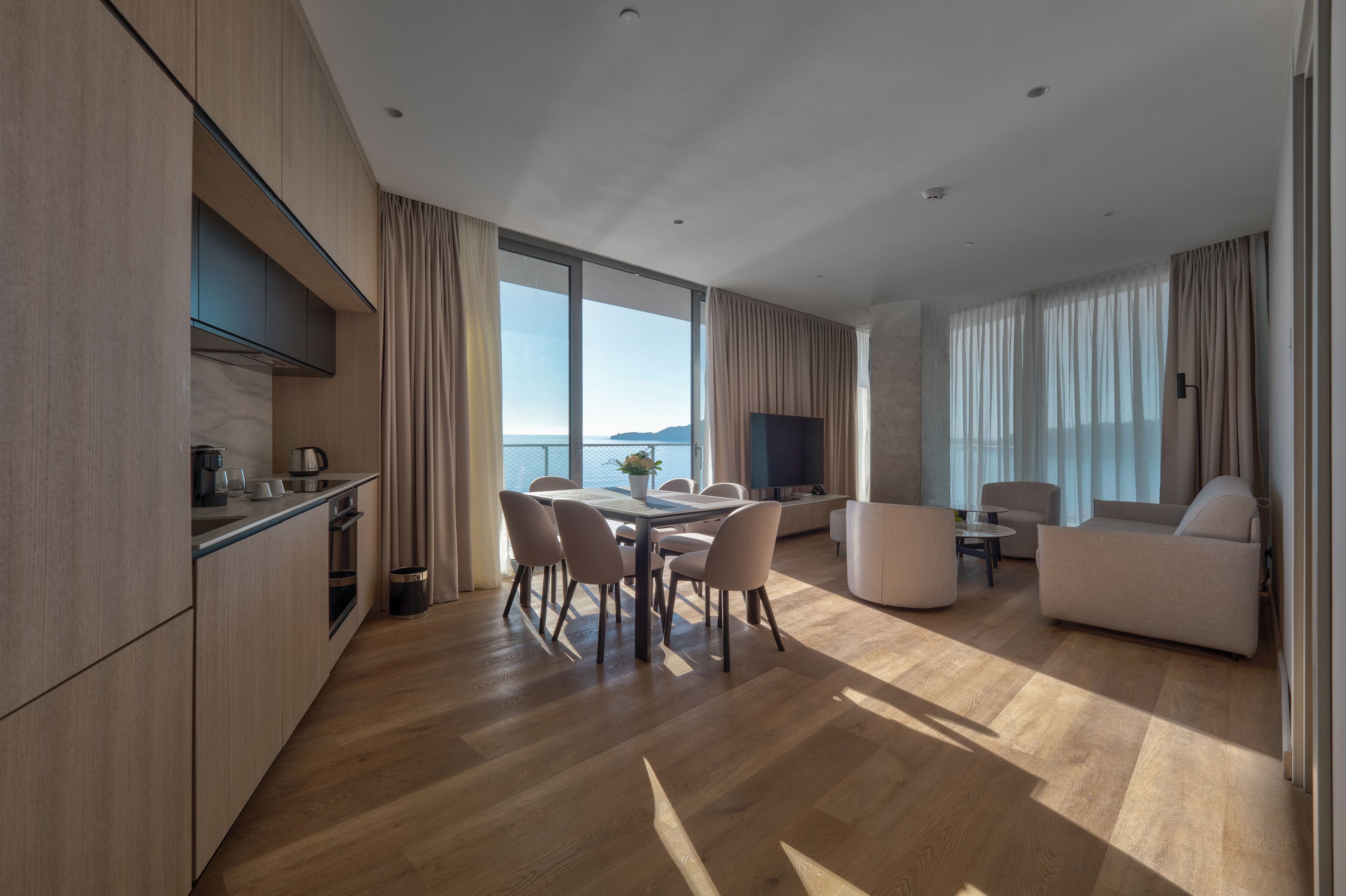 Una habitación de hotel moderna con zona de comedor, sofá y televisor.