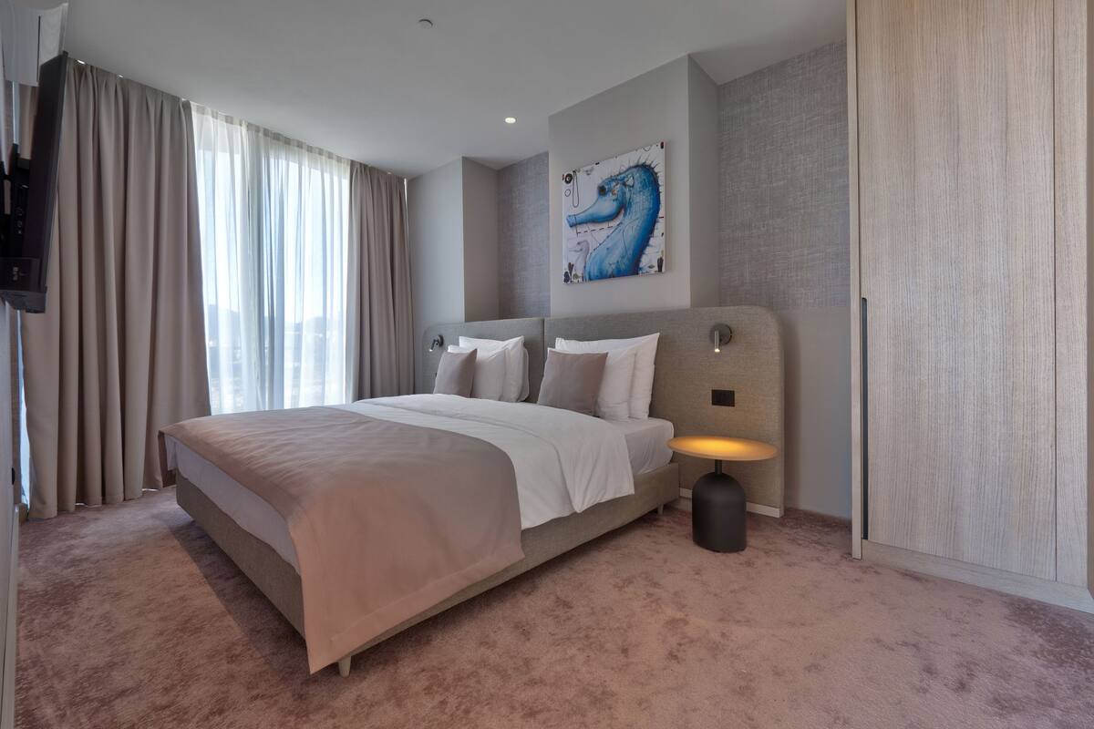 A modern hotel room with a large bed, a mounted TV, and a seahorse artwork on the wall.
