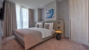 A modern hotel room with a large bed, a mounted TV, and a seahorse artwork on the wall.