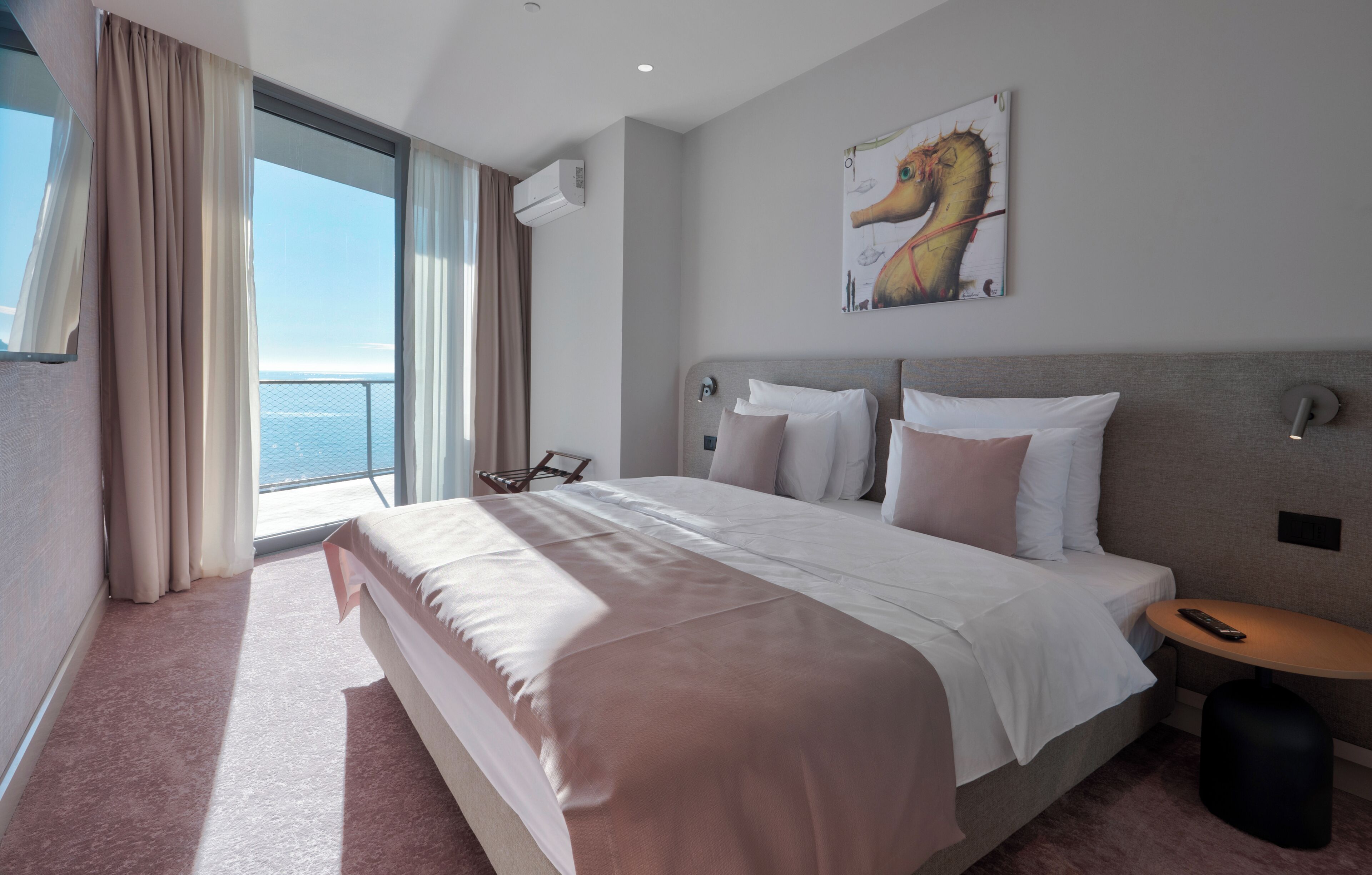 Ein Hotelzimmer mit einem großen Bett, Meerblick, einem Bild an der Wand und einem kleinen Tisch.