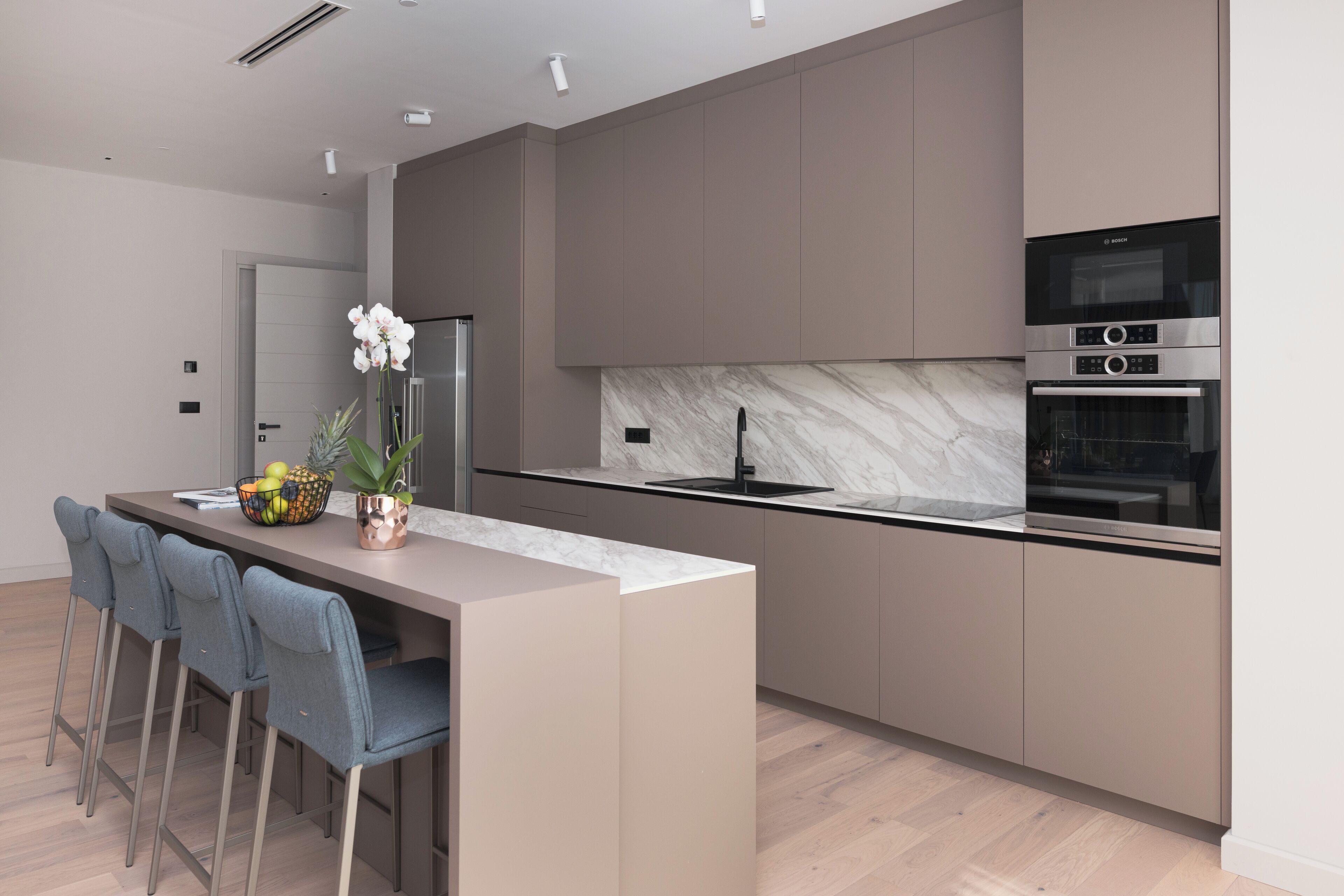 A modern kitchen with a marble backsplash, stainless steel appliances, and a central island with bar stools.