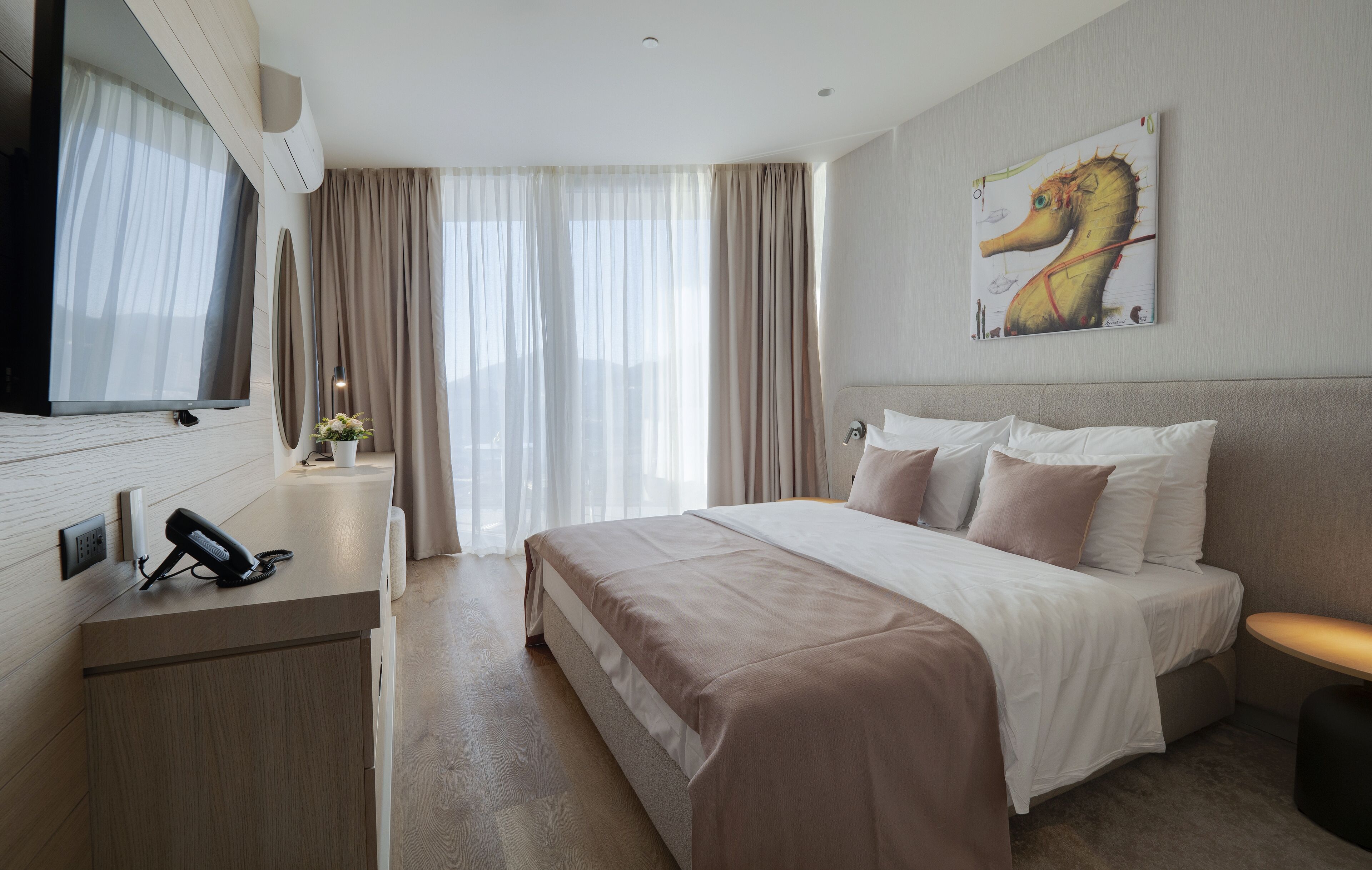 Quarto de hotel moderno com uma cama grande, televisão de tela plana, escrivaninha com telefone e um quadro na parede.
