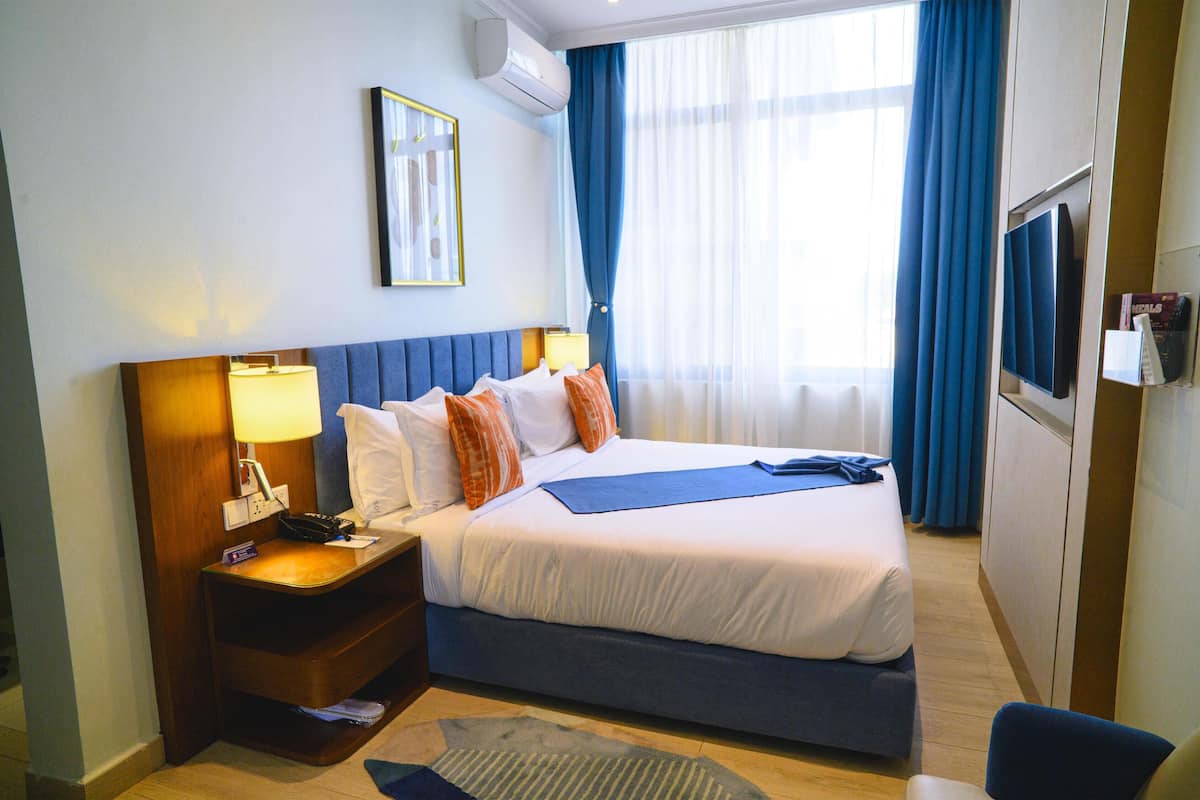 A hotel room with a bed, a nightstand, a TV, and a window with curtains.