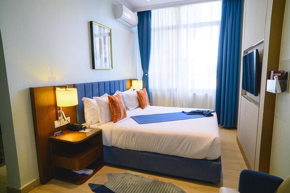 A hotel room with a bed, a nightstand, a TV, and a window with curtains.