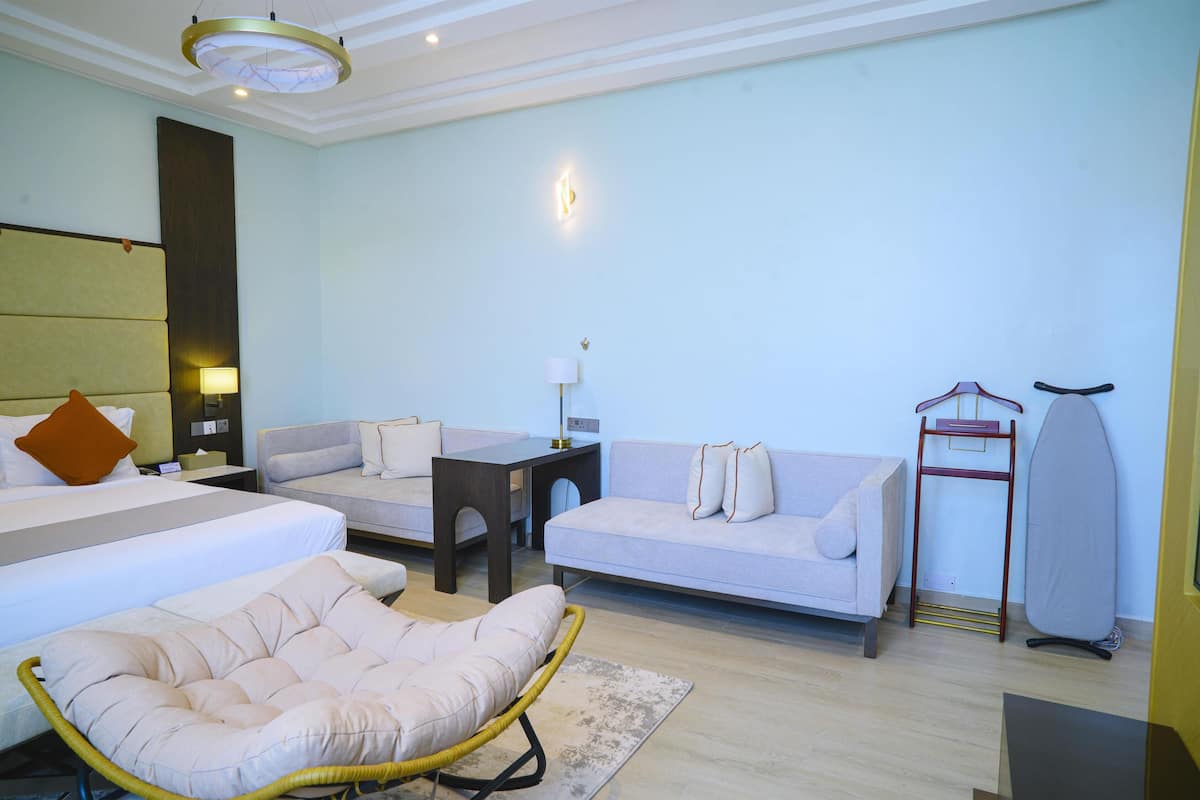A hotel room with a bed, two sofas, a chair, a table, a lamp, and an ironing board.