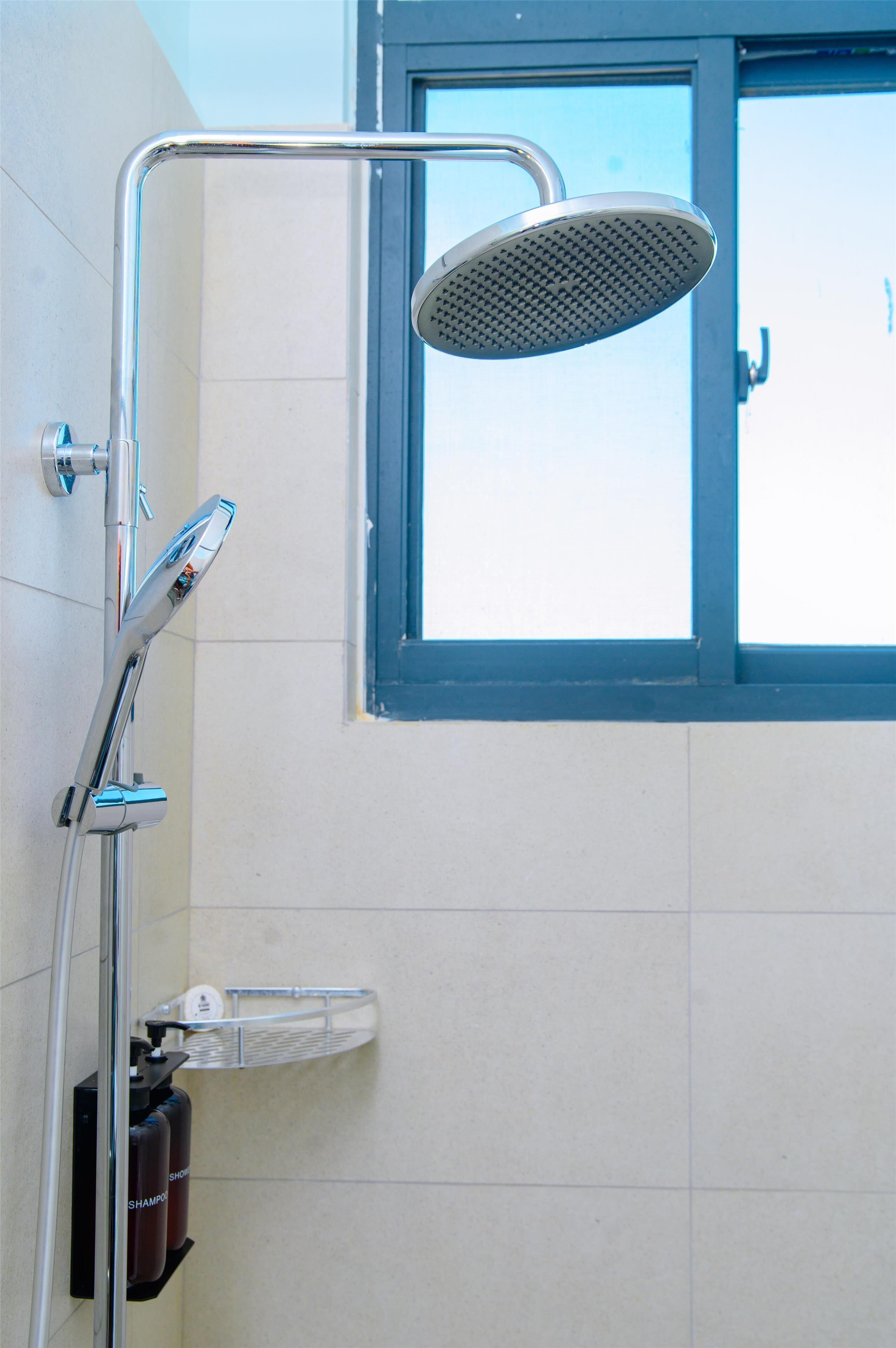 A shower area with a handheld showerhead, a wall-mounted faucet, and a window with a blue frame.