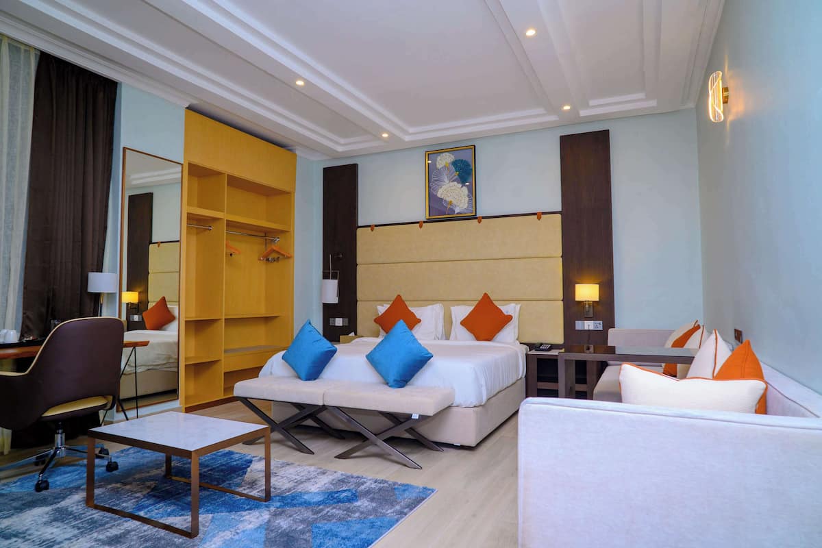 A hotel room with a bed, a sofa, a desk, a chair, a wardrobe, and a mirror.