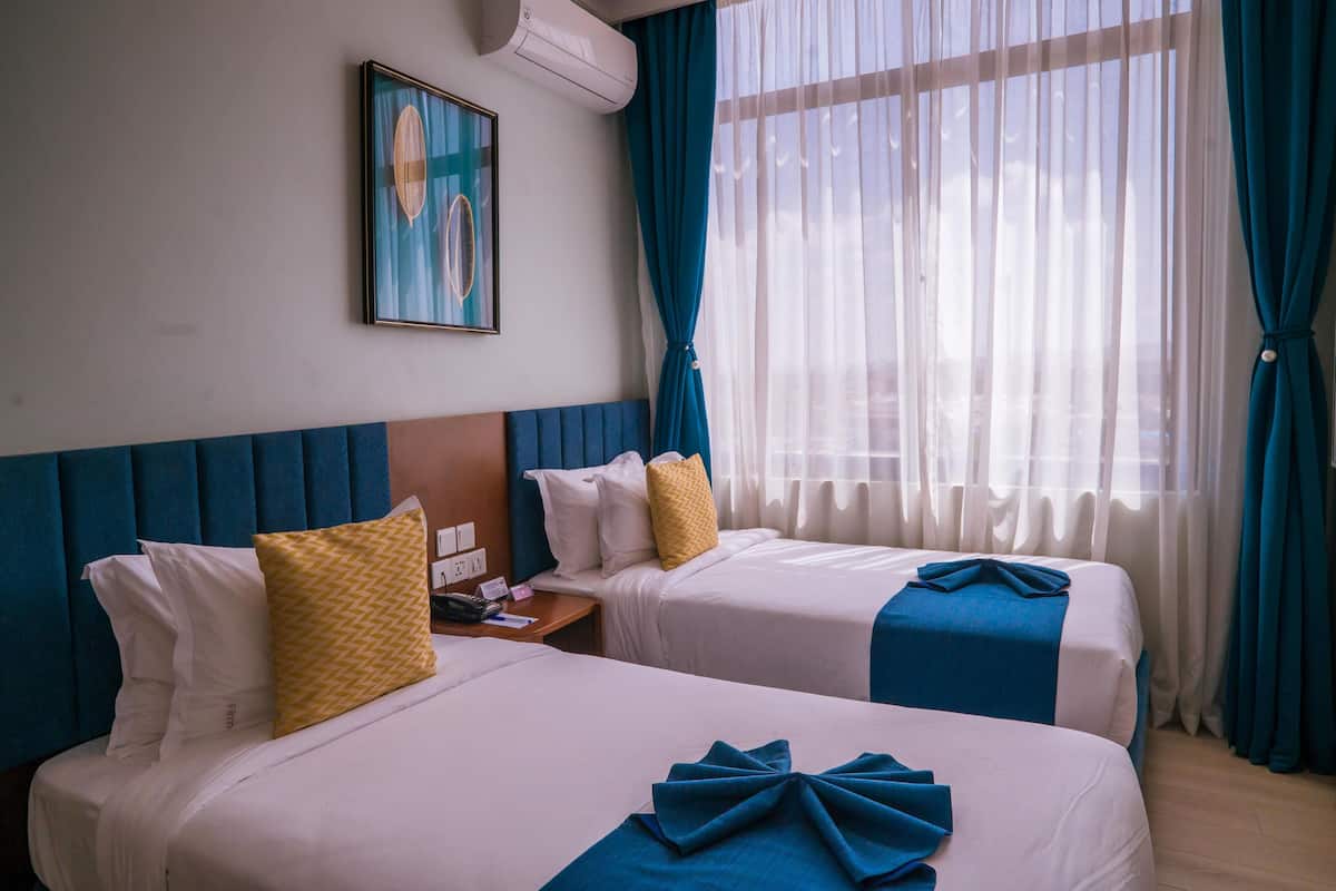 A hotel room with two beds, a painting on the wall, and a window with curtains.