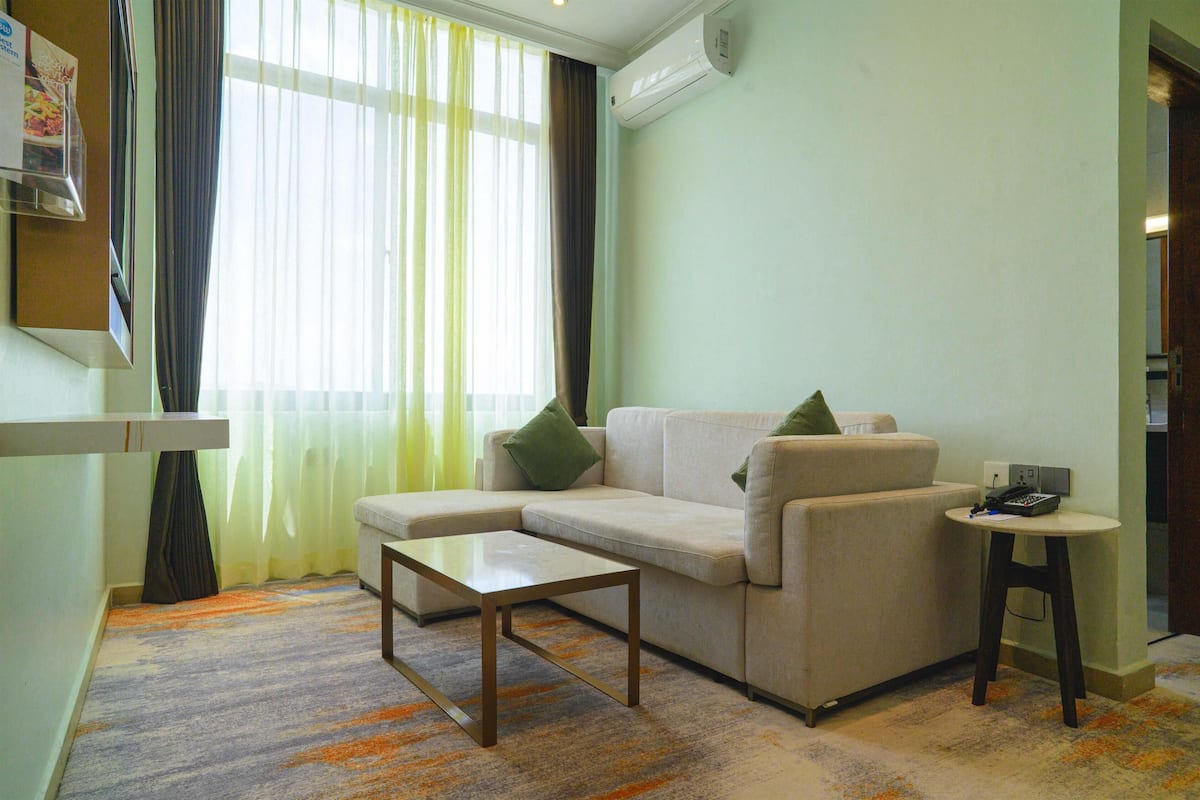 A living room with a sofa, a coffee table, a small side table, and a window with curtains.