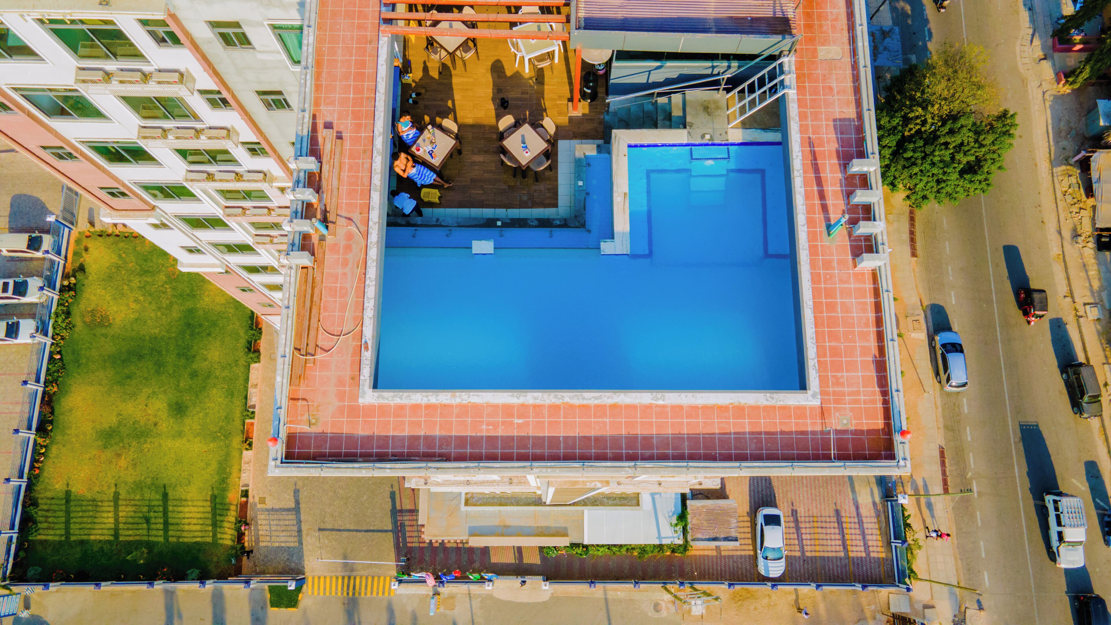 An aerial view of a hotel with a rooftop pool, outdoor seating area, and a parking lot.