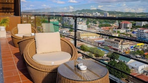 Un balcón con mobiliario de mimbre, una planta en maceta y vistas a la ciudad.