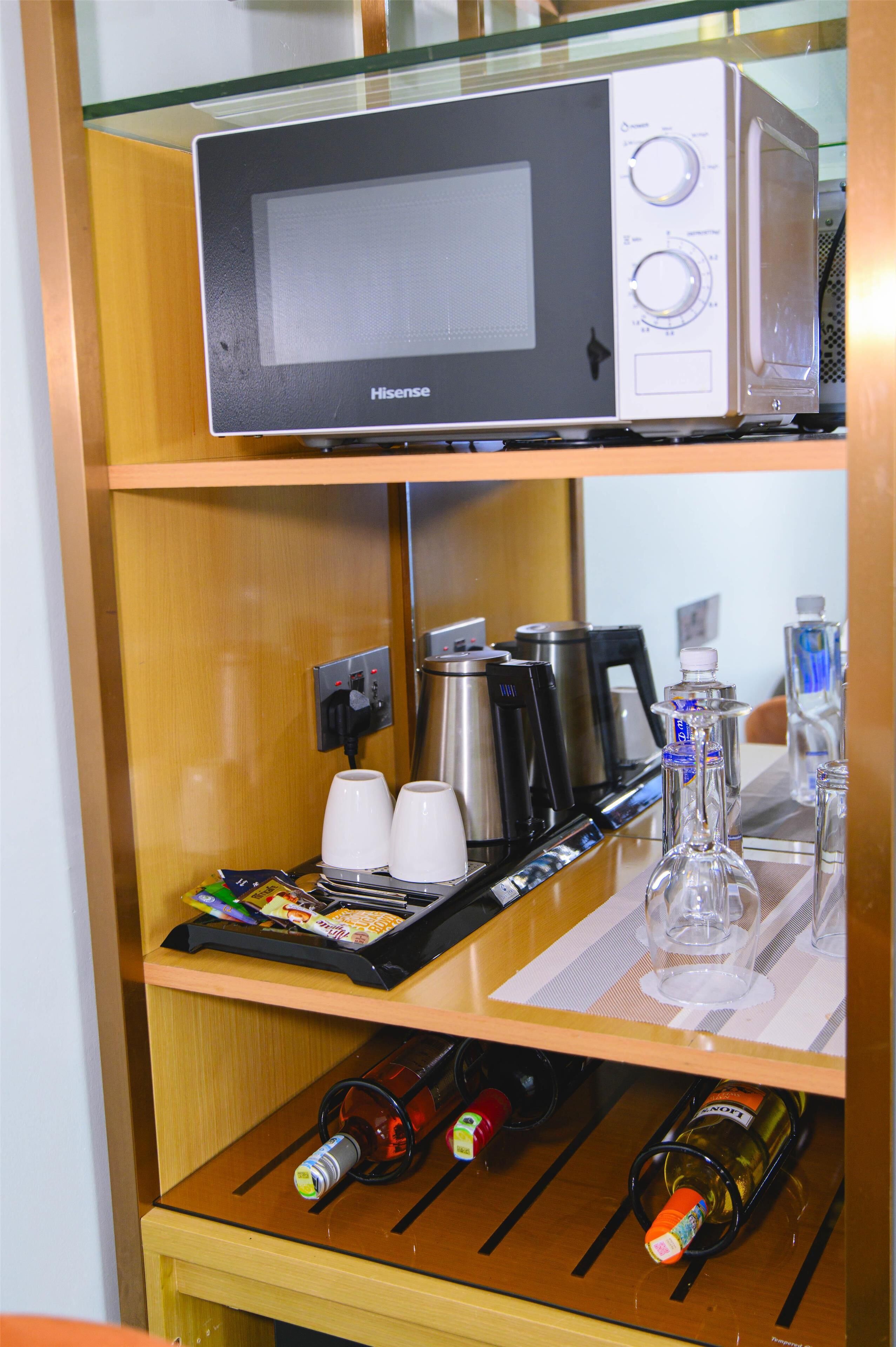 A microwave on a shelf, a coffee maker, cups, a wine bottle, and a wine glass.