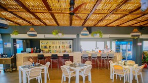Un restaurante con techo de bambú, sillas blancas y una zona de bar con diversas botellas.