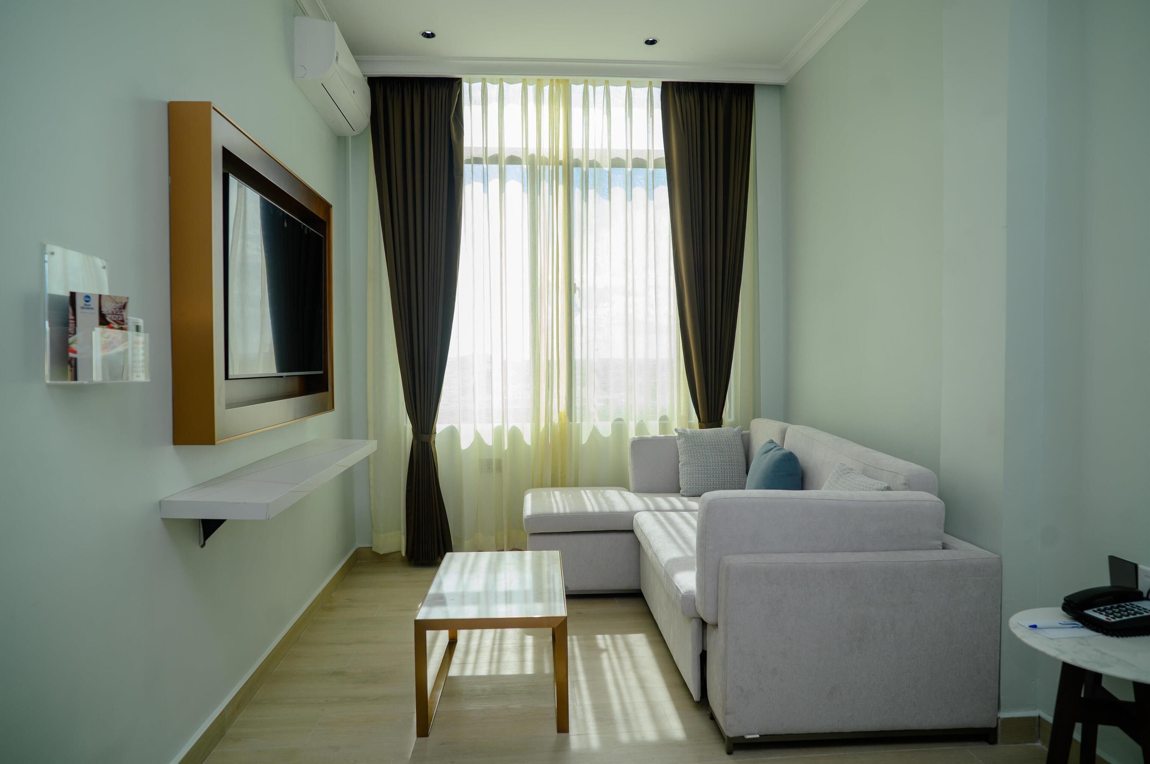 A modern living room with a flat-screen TV, a sofa, a coffee table, and a small table with a phone and pen.