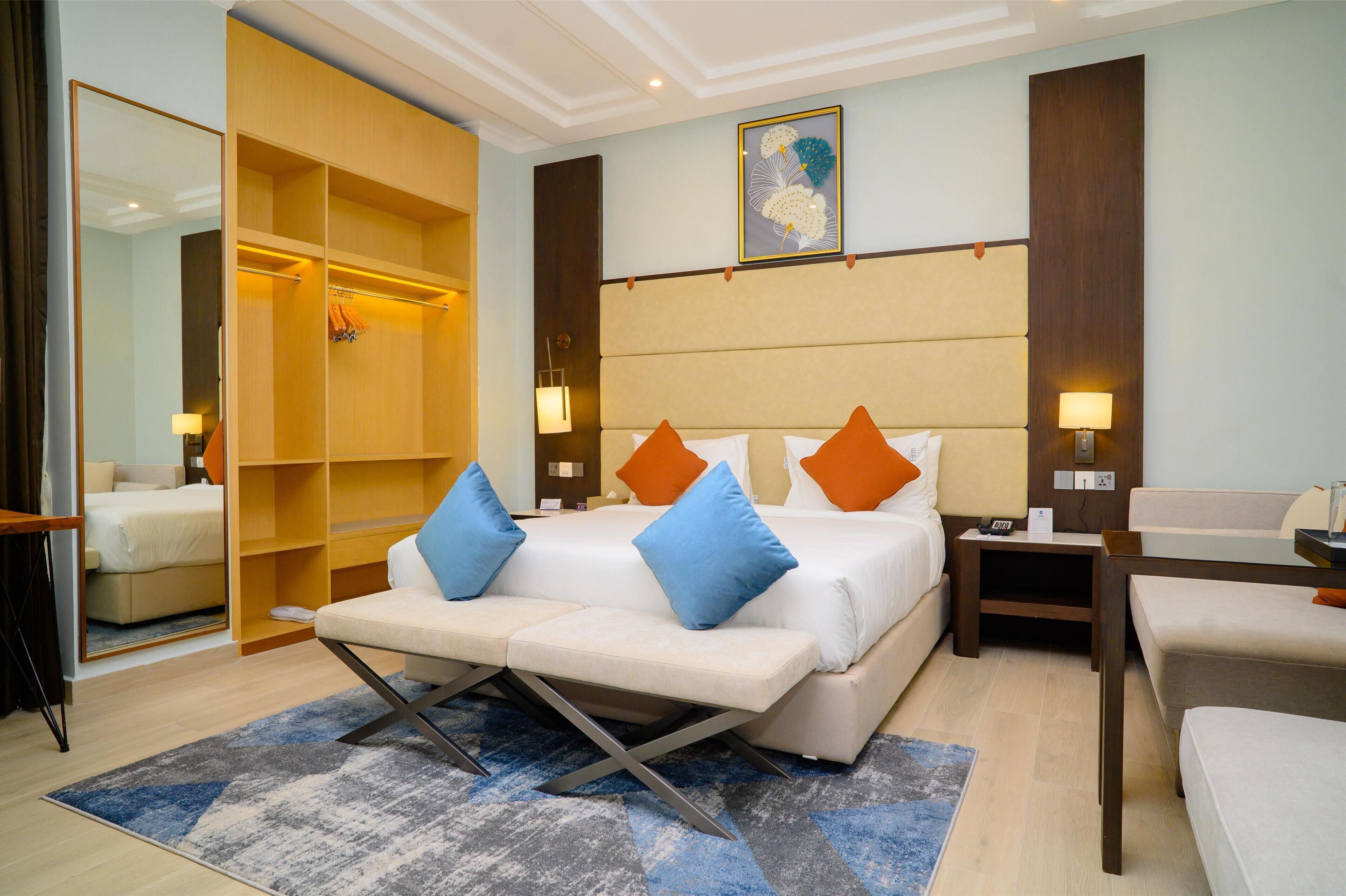 Una habitación de hotel con una cama grande, un área de estar, un armario y un cuadro en la pared.