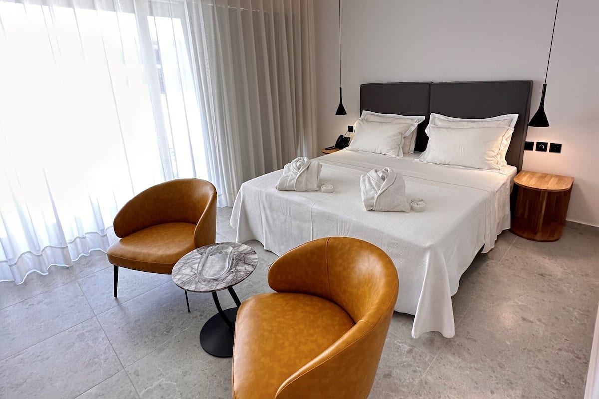 Moderni hotellihuone, jossa on suuri sänky, kaksi nojatuolia, pieni pyöreä pöytä ja yöpöytä.