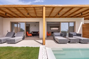Un moderno espacio lounge al aire libre con dos zonas de estar, una piscina y un porche cubierto.