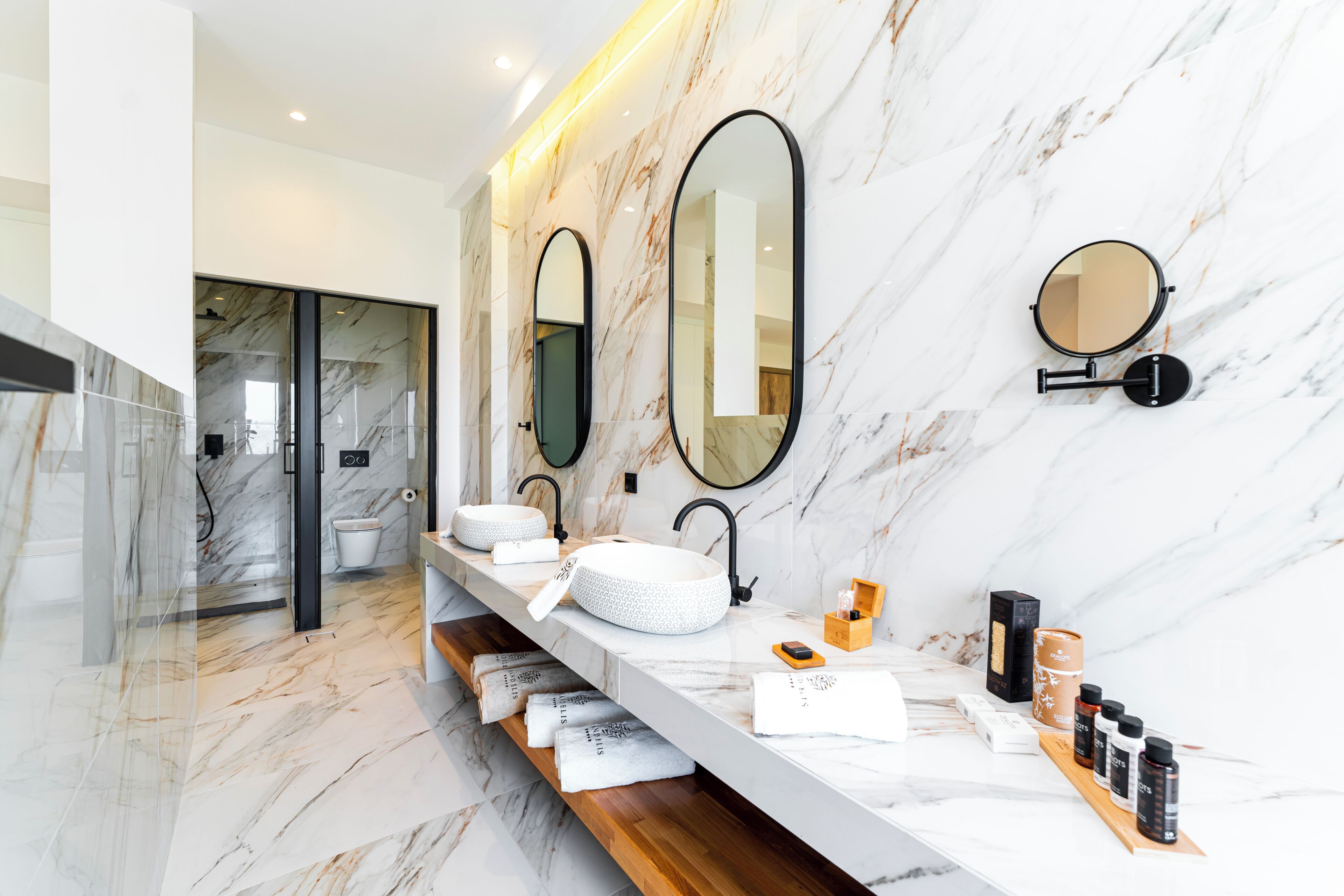 Une salle de bain moderne avec des murs en marbre, trois lavabos et de nombreux miroirs.
